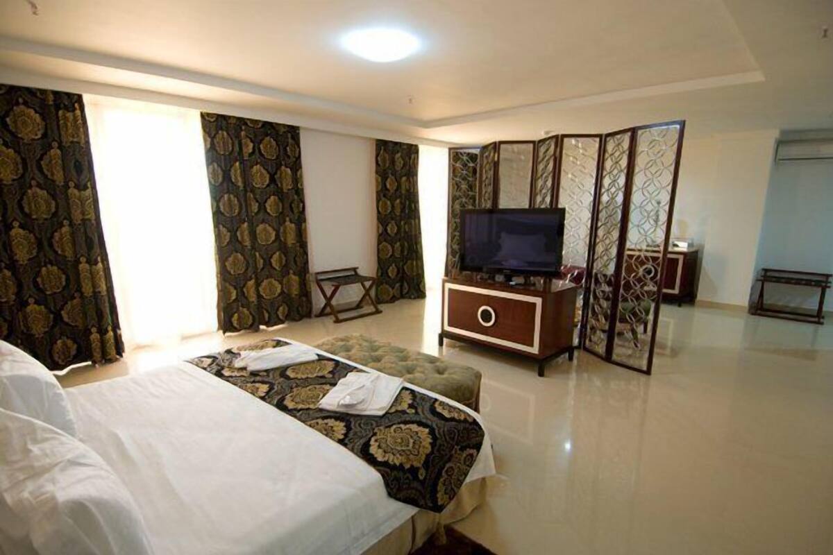 A hotel room with a bed, a TV, a wooden cabinet, and a decorative screen.