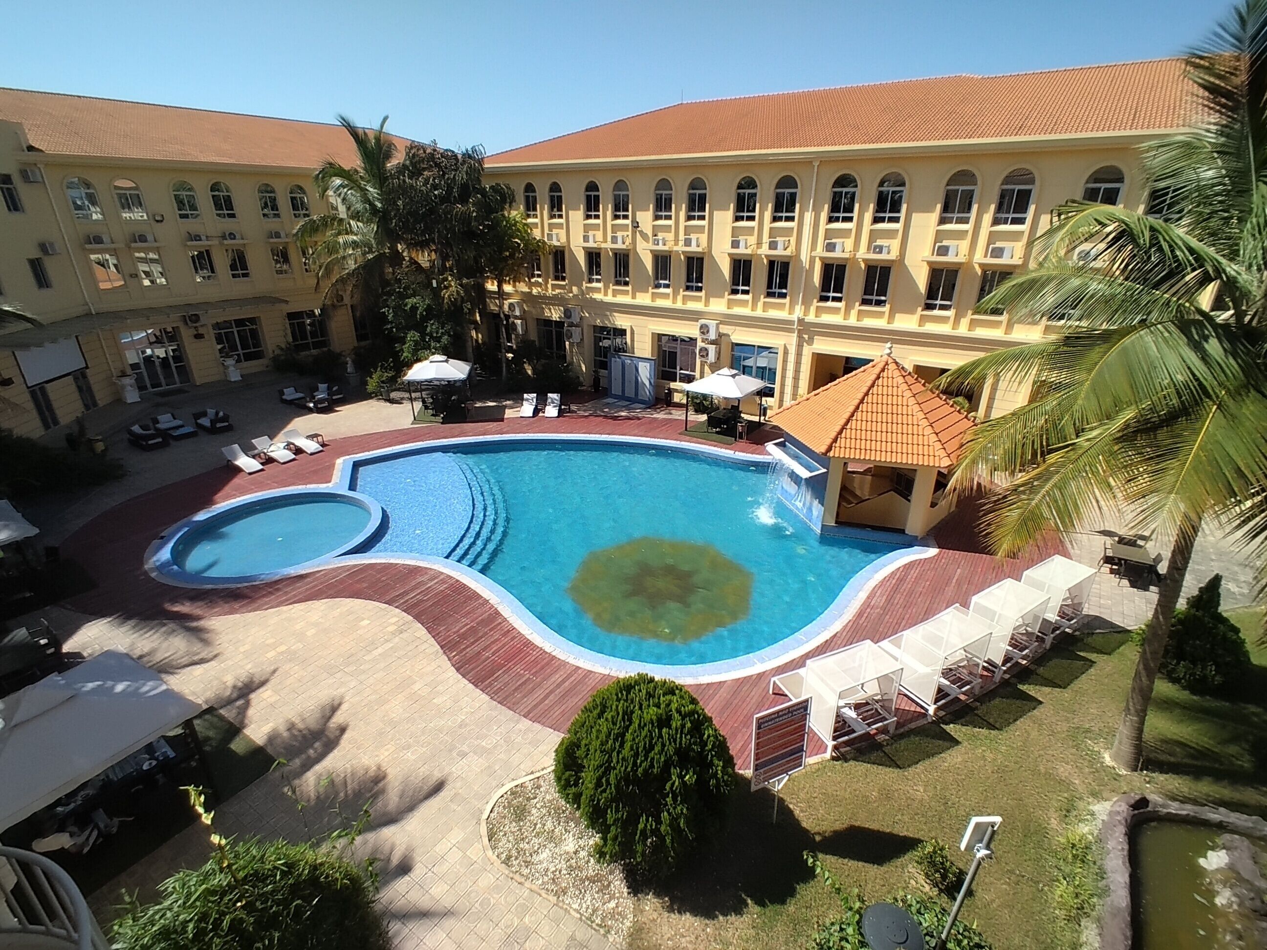 Un hotel con una piscina grande, sillas de sol y una zona cubierta.