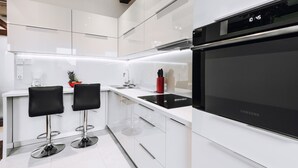 A modern kitchen with white cabinetry, two black bar stools, a stainless steel sink, and a Samsung oven. - EchoDom 4 Apartments Szlak (Kraków)