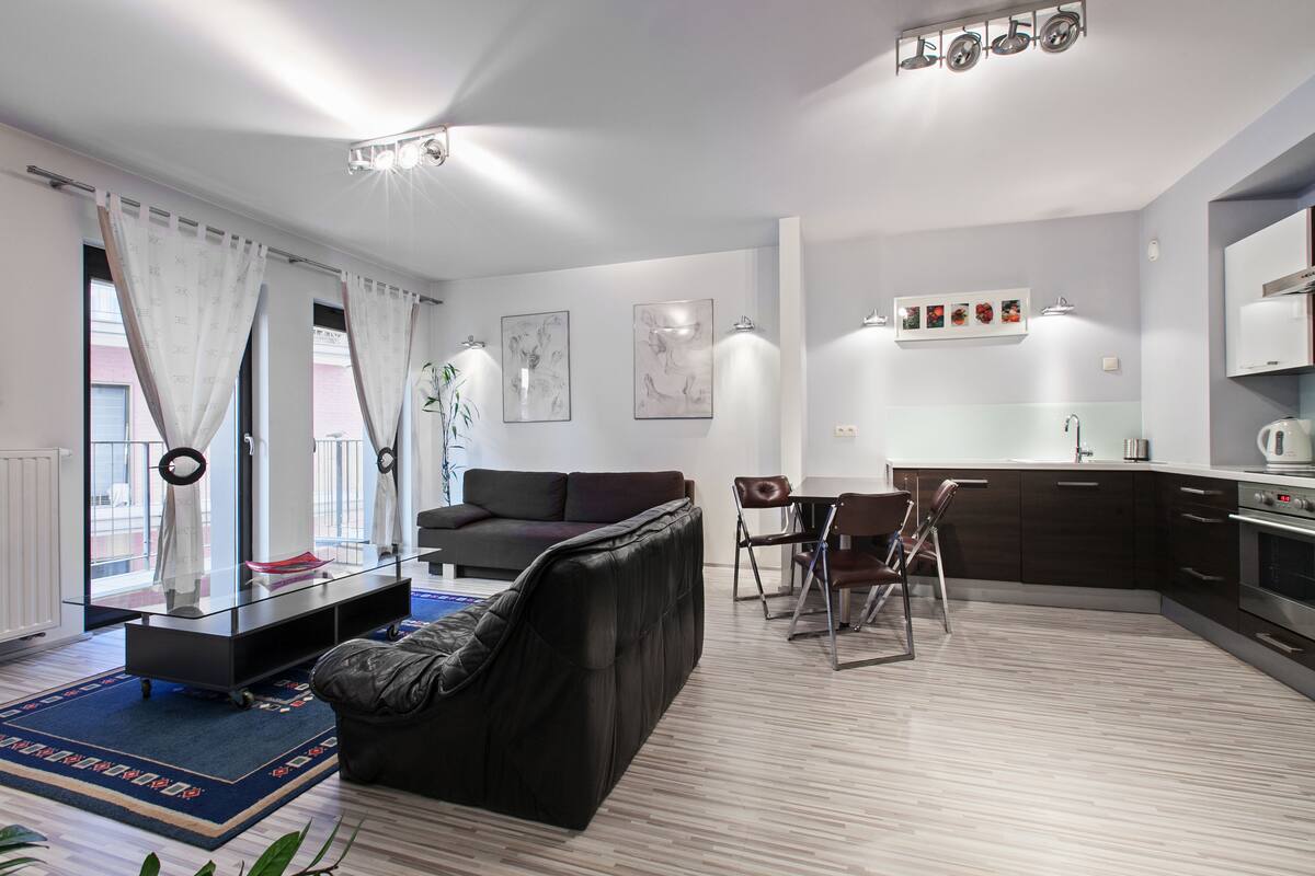 A modern living room with a sofa, a dining table, and a kitchen area.