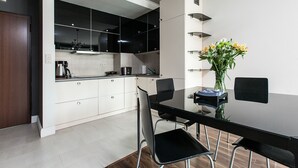A modern kitchen with white cabinets, a black countertop, and a dining table with chairs. - EchoDom 4 Apartments Szlak (Kraków)