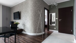 A modern dining area with a curved wall, a flat-screen TV, a dining table with chairs, and a decorative vase. - EchoDom 4 Apartments Szlak (Kraków)