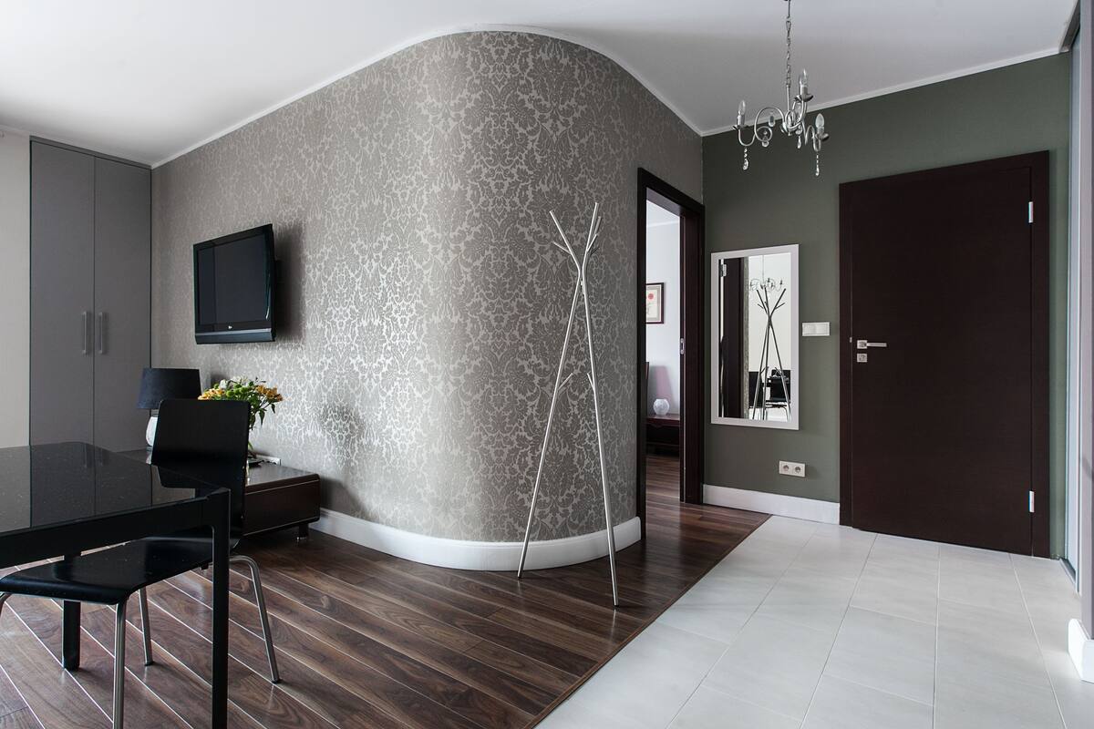 A modern dining area with a curved wall, a flat-screen TV, a dining table with chairs, and a decorative vase.