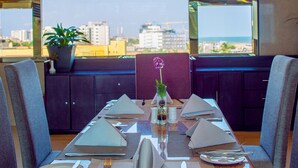 A dining table set for six with a city view, potted plants, and a vase with a flower. - BWC Hotel (Lagos)