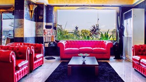 A red leather sofa set in a modern living room with a black rug, a coffee table, and a view of a garden through a large window. - BWC Hotel (Lagos)