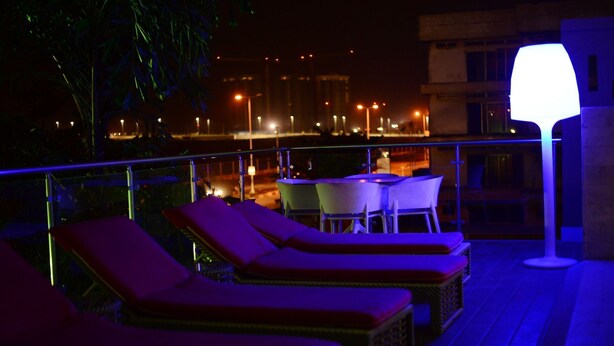 A rooftop terrace with sun loungers and a table, overlooking a cityscape at night. - BWC Hotel (Lagos)
