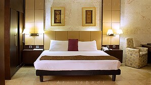 A hotel room with a large bed, two bedside lamps, a chair, and a wall clock. - BWC Hotel (Lagos)