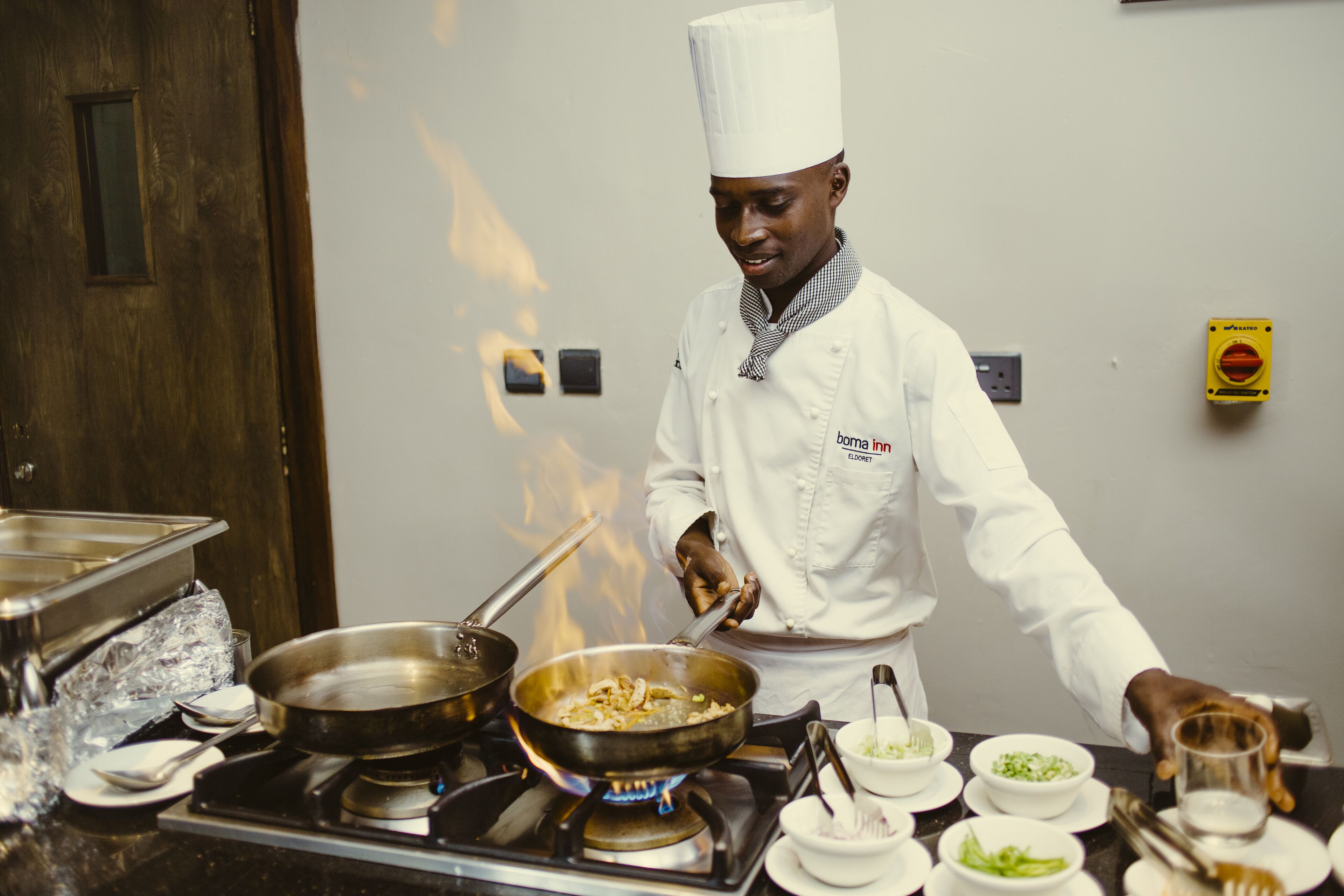 A chef in a white uniform cooking on a stove with a pan.