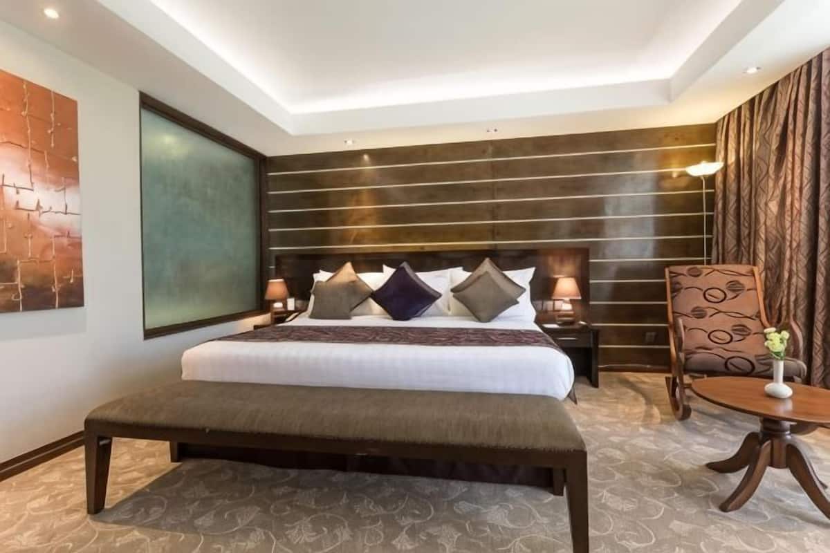 Una habitación de hotel moderna con una cama grande, un banco, una silla y una mesita.