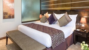 A modern hotel room with a large bed, a bench, a nightstand with a lamp, and a wall with abstract art.