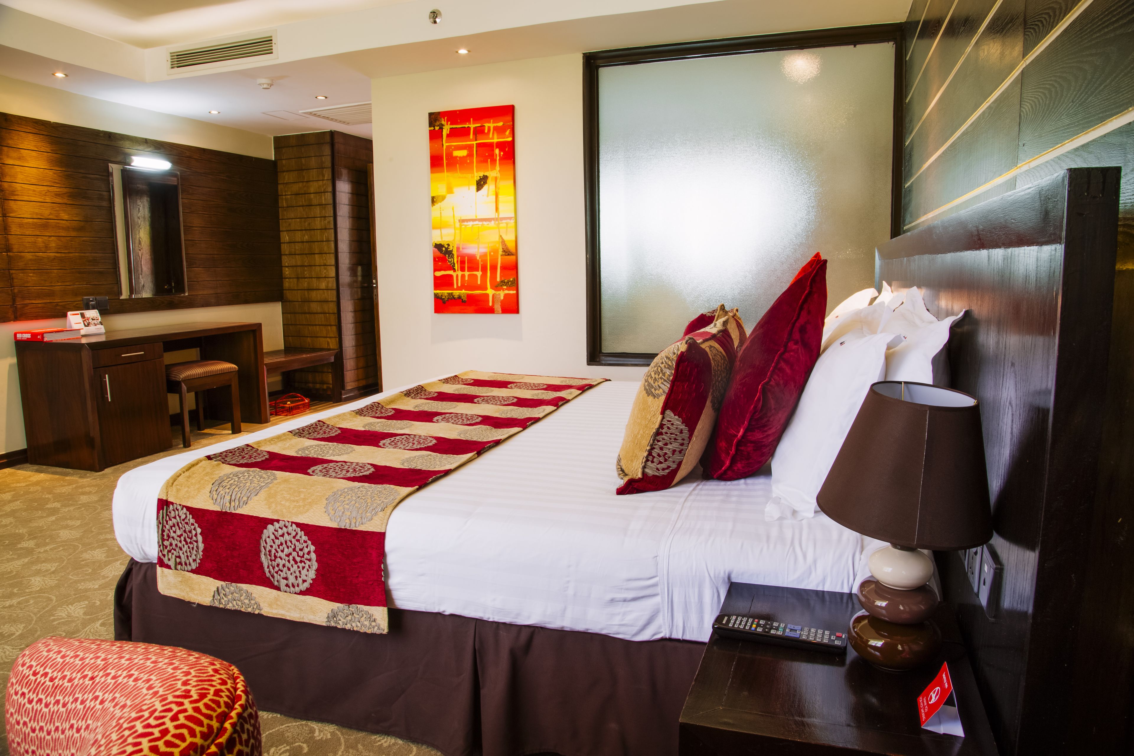 A hotel room with a large bed, a desk, a chair, a lamp, and a painting on the wall.