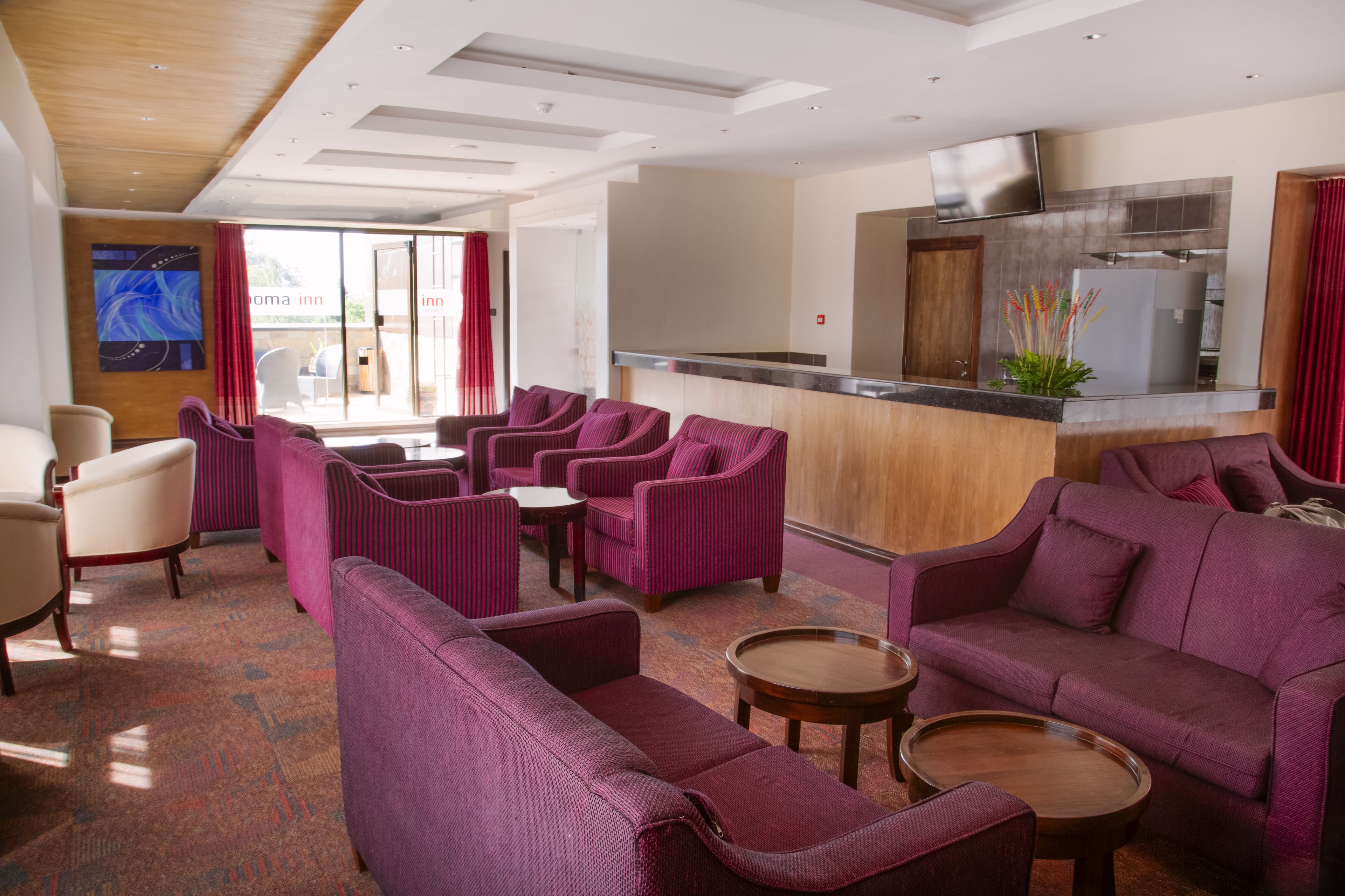 A hotel lobby with purple sofas, a reception desk, and a kitchen area.