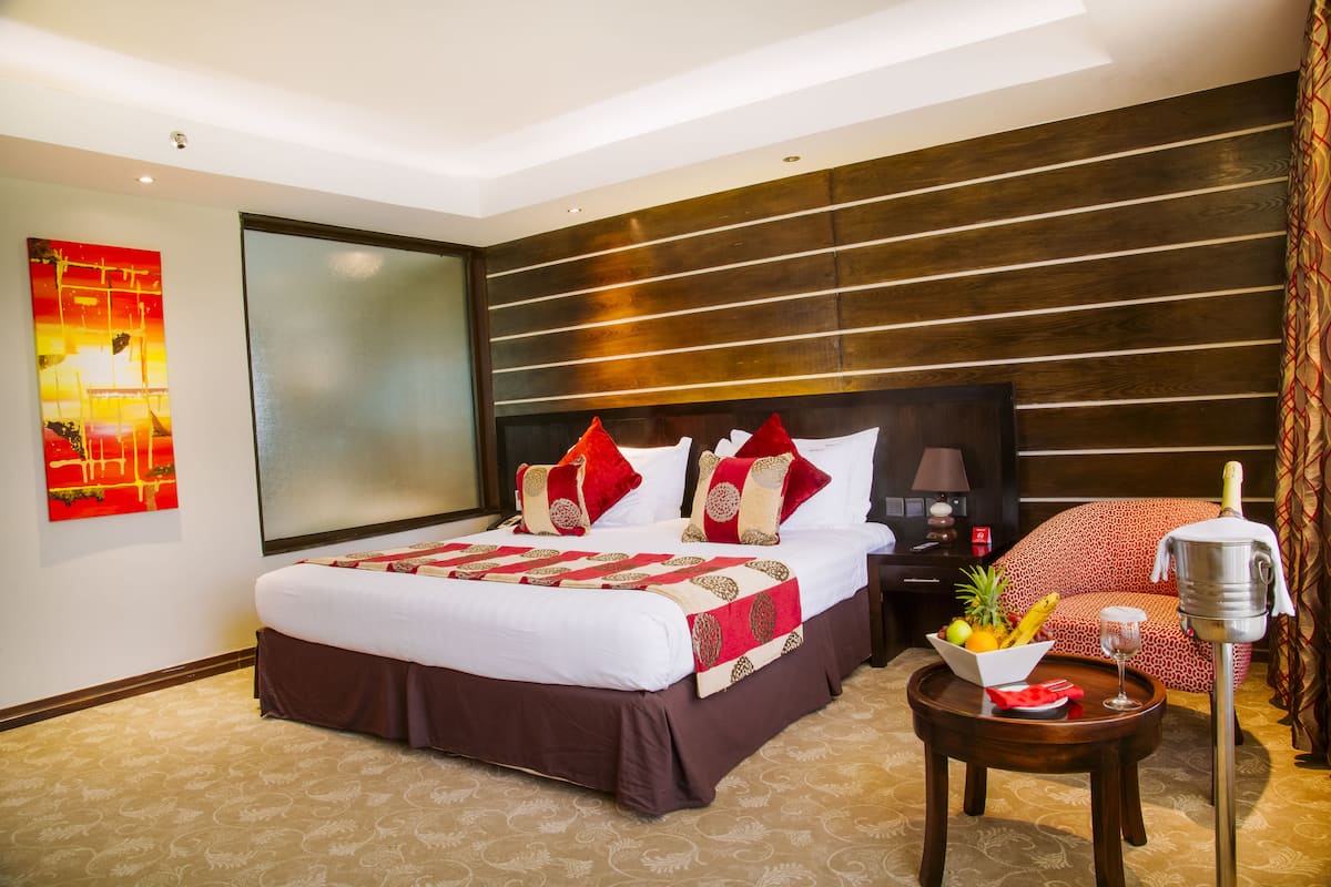 Habitación de hotel con una cama grande, una mesita de noche con frutero, una botella de champán y una silla de diseño rojo y blanco.