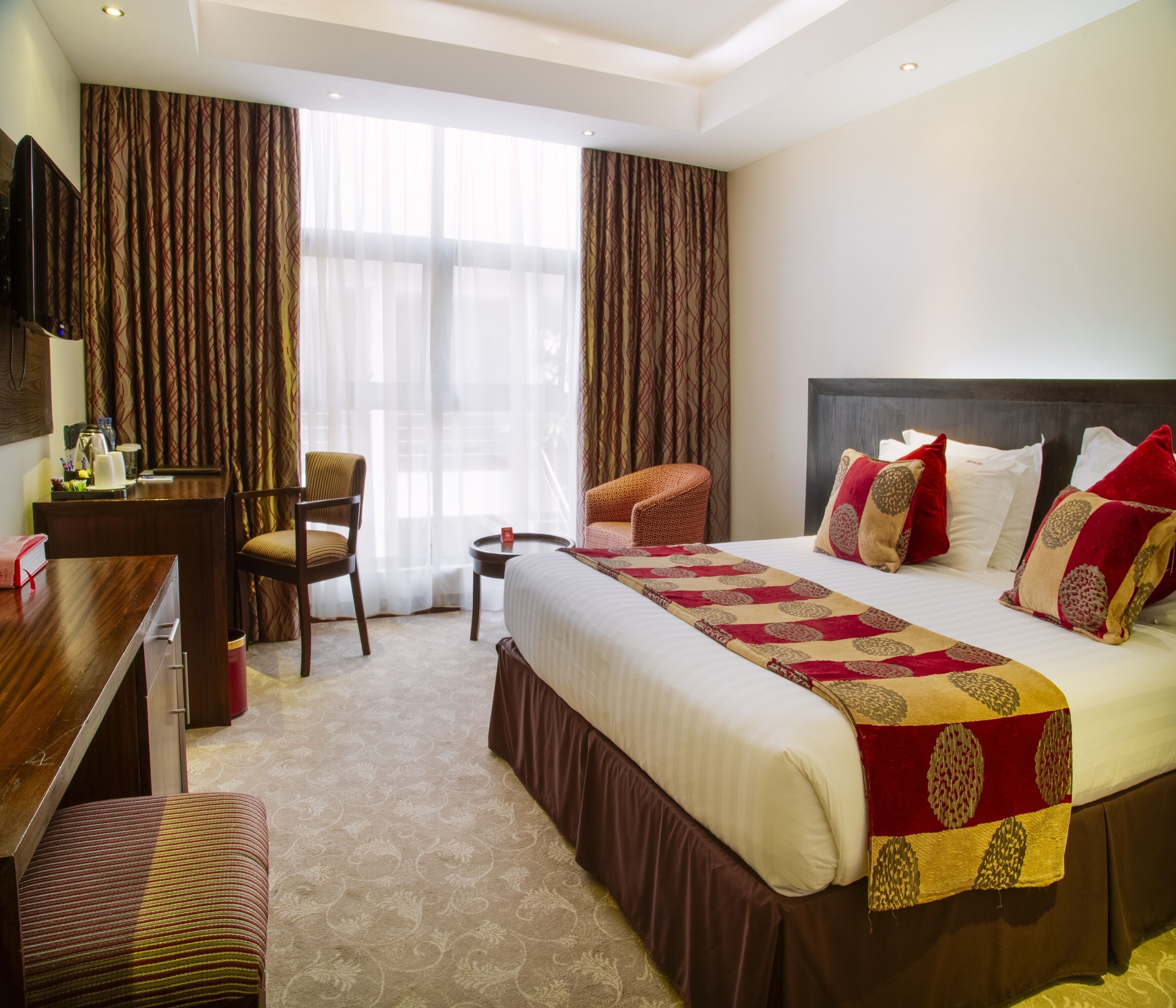 A hotel room with a large bed, a desk, a chair, and a television.