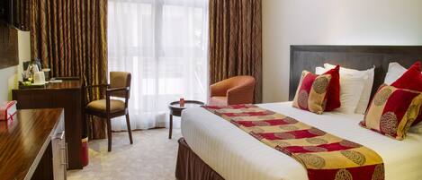 A hotel room with a large bed, a desk, a chair, and a television.