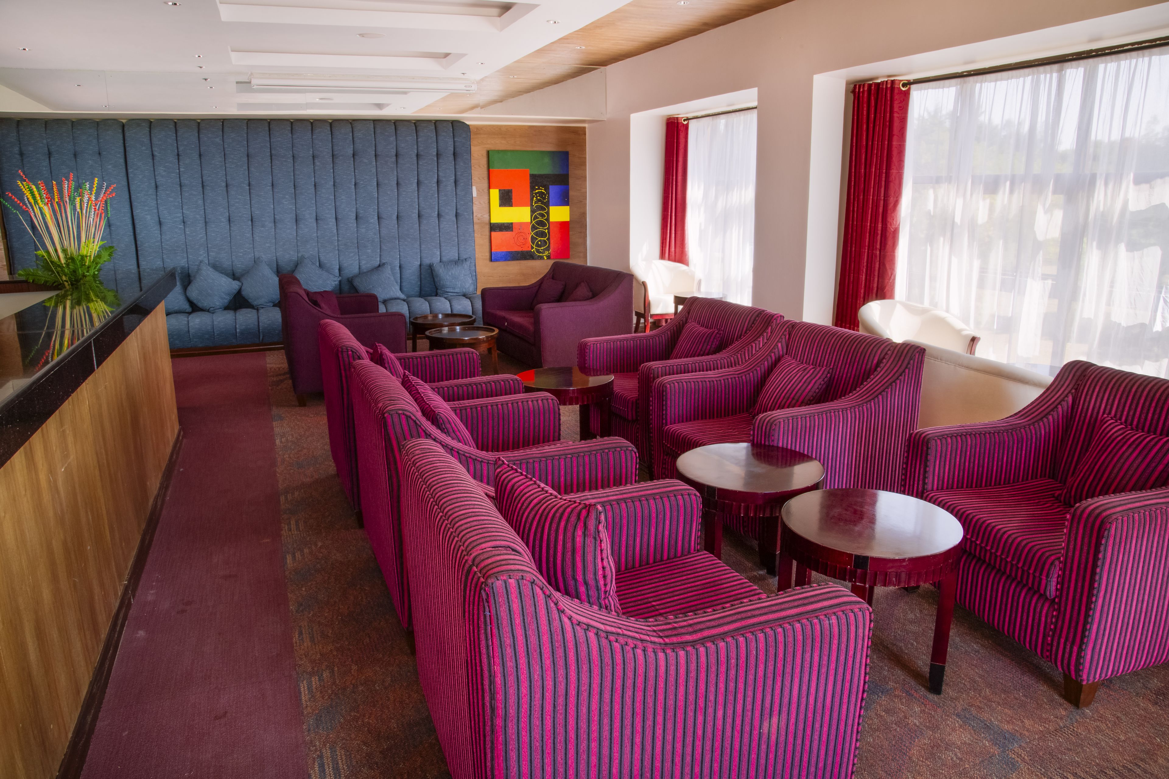 Un espace de détente moderne avec des canapés et des fauteuils à rayures, un mur rembourré bleu et une œuvre d’art abstraite aux couleurs vives.