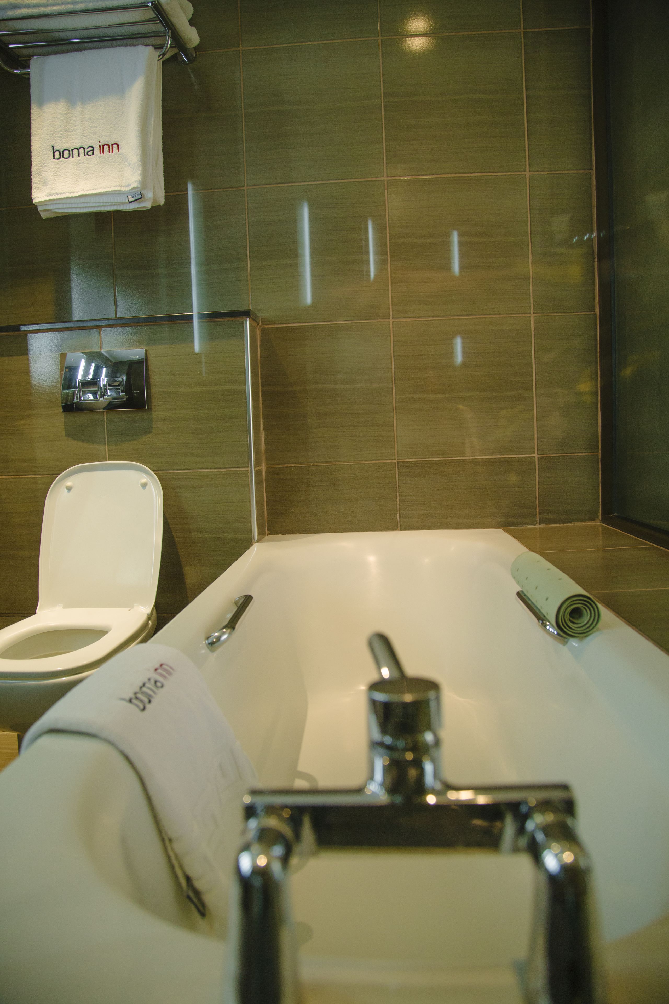 A bathroom with a toilet, a bathtub, and a towel rack with a 'boma inn' towel.