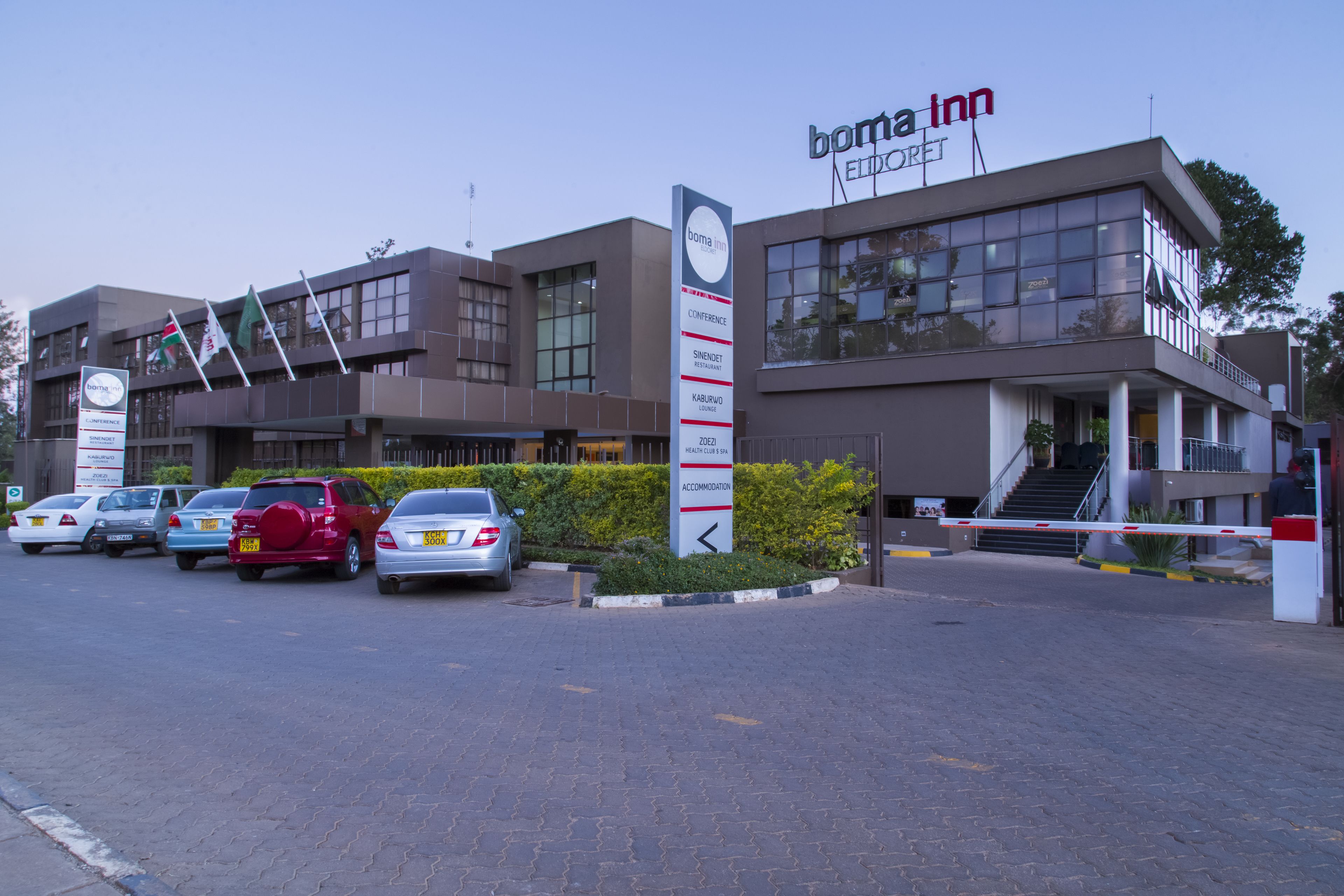 A modern building with a 'boma inn' sign, multiple flags, and a parking area with several cars.