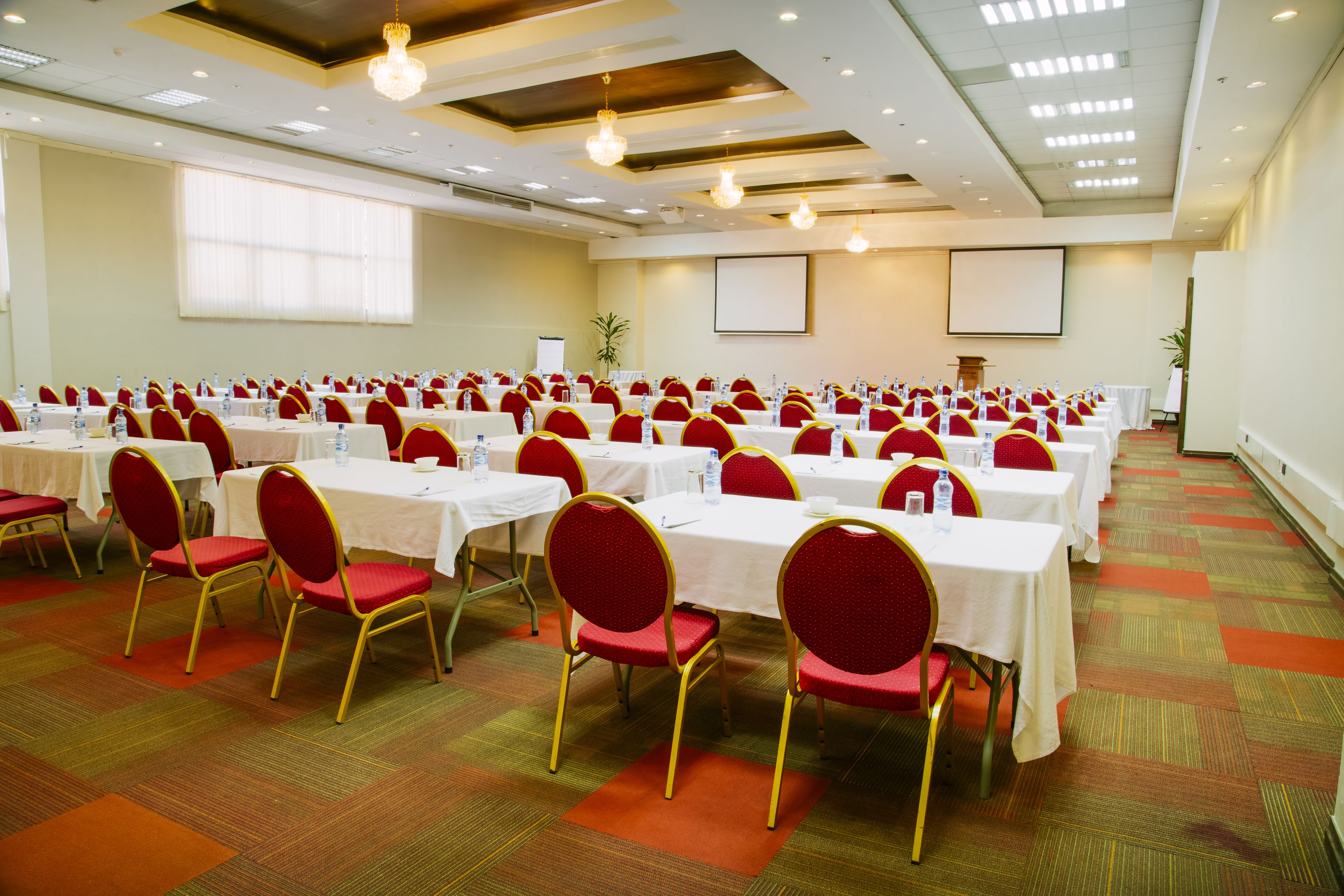 A conference room with rows of tables and chairs, a projector screen, and a podium.