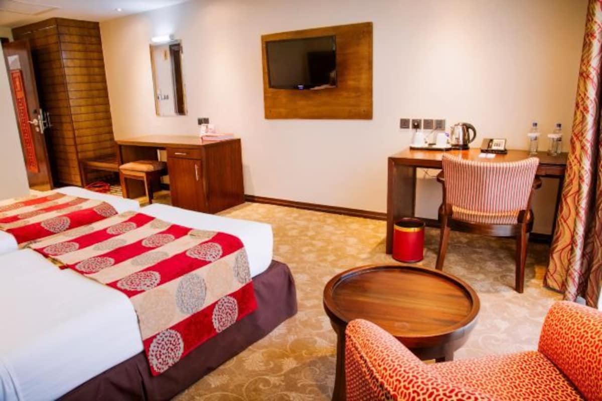 Una habitación de hotel con cama, escritorio, silla, televisor y una mesita.