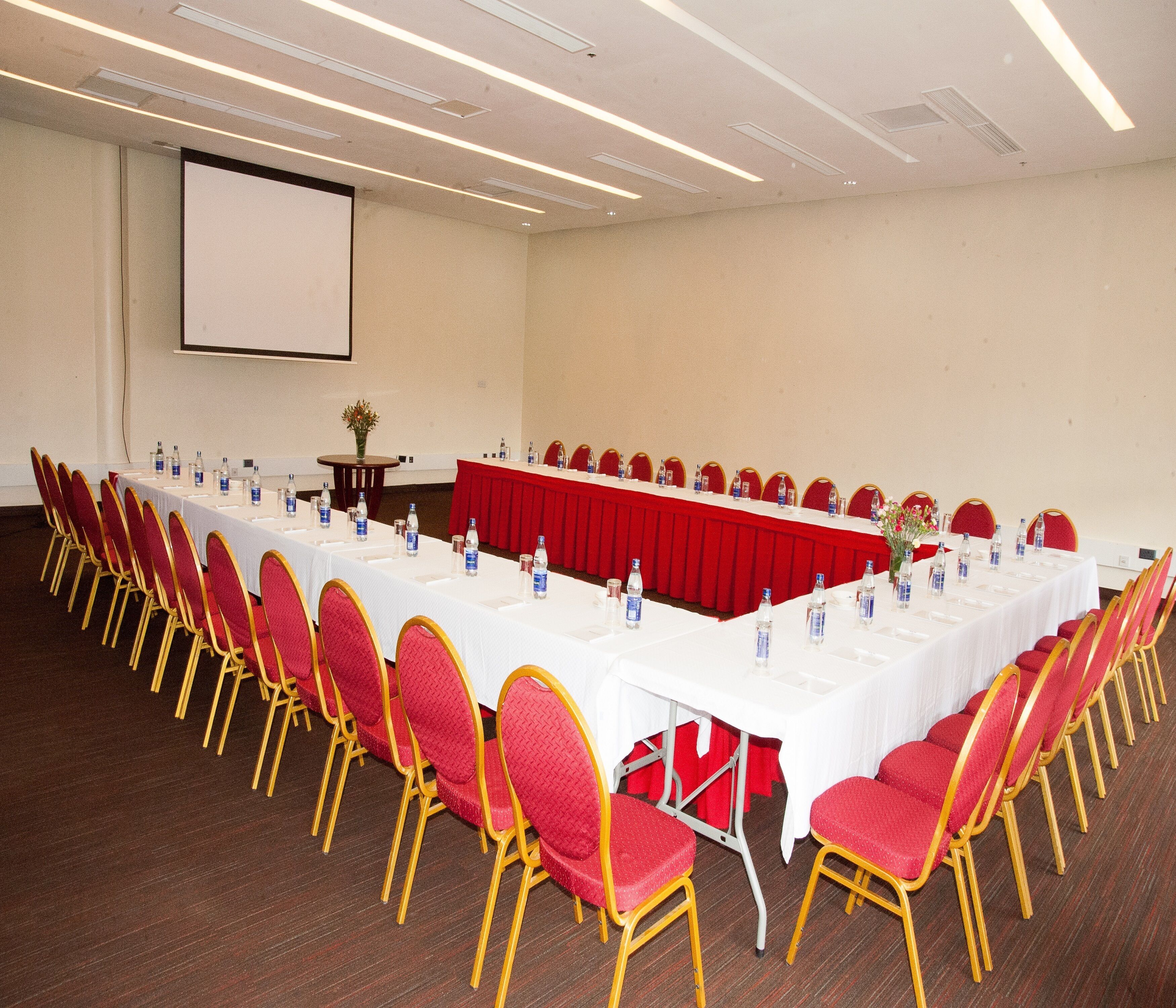 Une salle de conférence avec une longue table, des chaises rouges et des bouteilles d’eau.