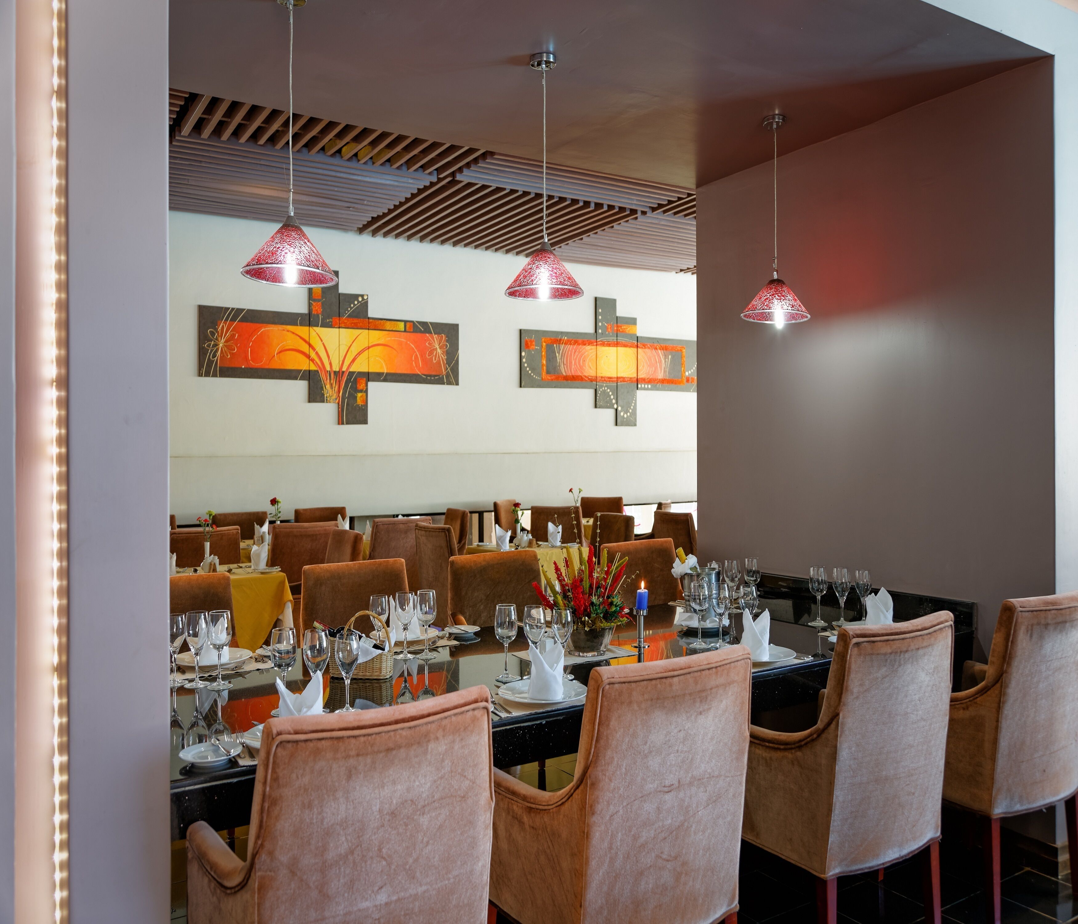 A restaurant with multiple tables set for dining, featuring brown upholstered chairs and red pendant lighting.