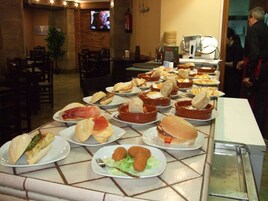 Una mesa de buffet con diferentes alimentos y un televisor al fondo.
