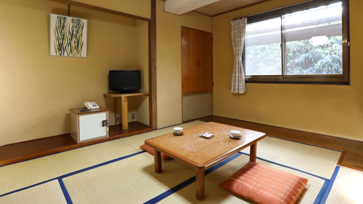 A traditional Japanese room with tatami flooring, a low wooden table with cushions, a television on a stand, and a cabinet with a telephone.