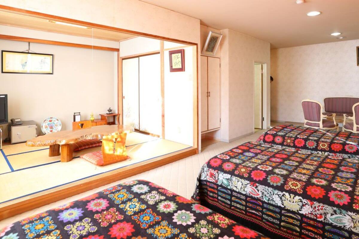 Une chambre d’hôtel avec des tatamis au sol, un futon, une télévision, une armoire et une porte coulissante de style japonais traditionnel.