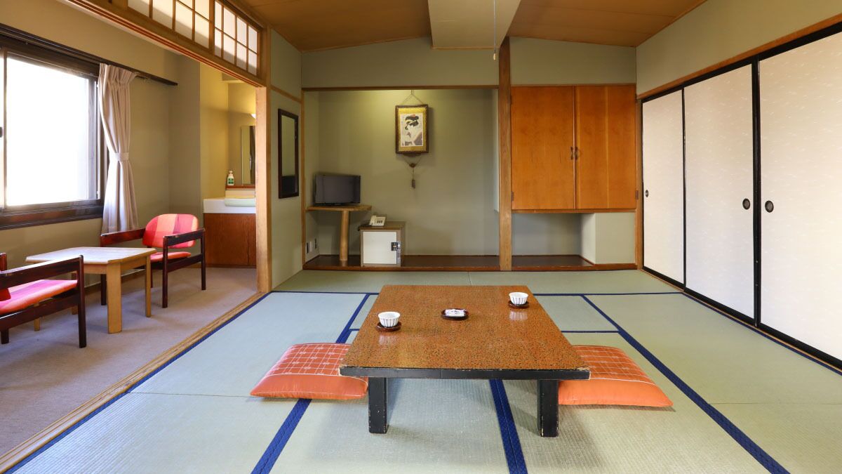A traditional Japanese room with tatami flooring, a low table with cushions, a television, and sliding doors.