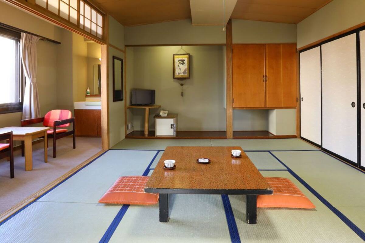 Une pièce de style japonais traditionnel, avec un sol recouvert de tatamis, une table basse avec des coussins, un téléviseur et des portes coulissantes.