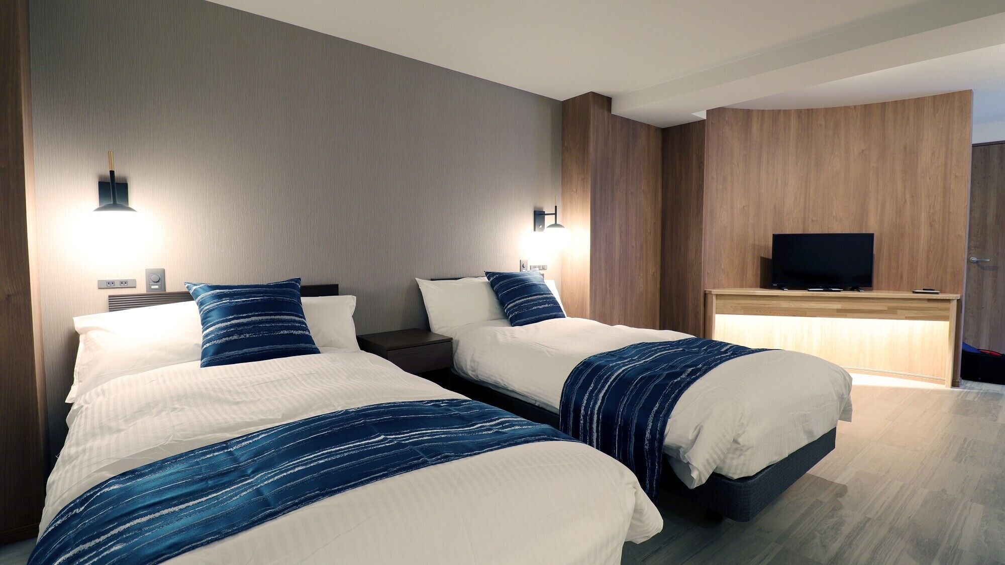 A hotel room with two beds, a TV, and a desk.