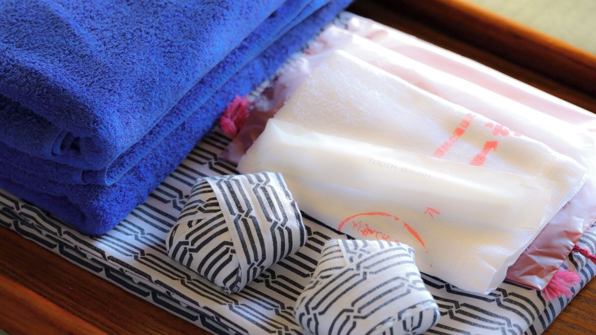 A stack of blue towels, a bar of soap, and striped bathrobes on a patterned cloth.