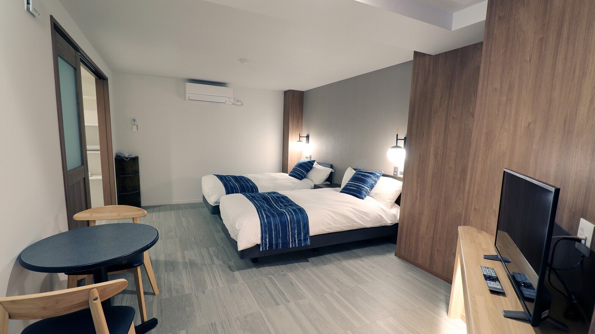 A hotel room with two beds, a desk with a computer, a chair, and a small table.