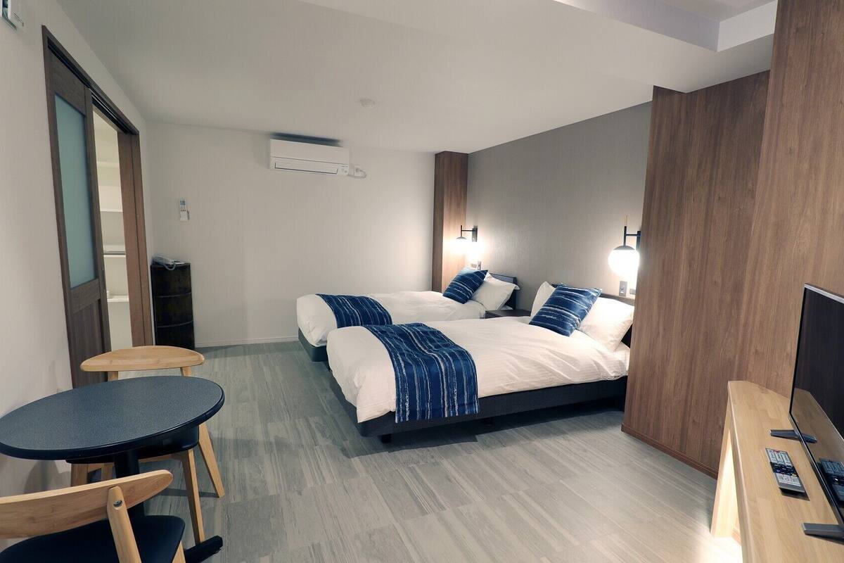 Une chambre d’hôtel avec deux lits, un bureau avec un ordinateur, une chaise et une petite table.
