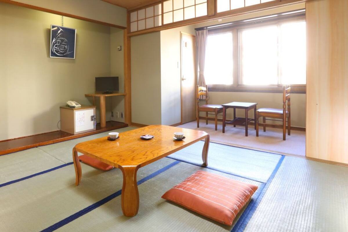 Une pièce de style japonais traditionnel, avec un sol recouvert de tatamis, une table en bois et un téléviseur.