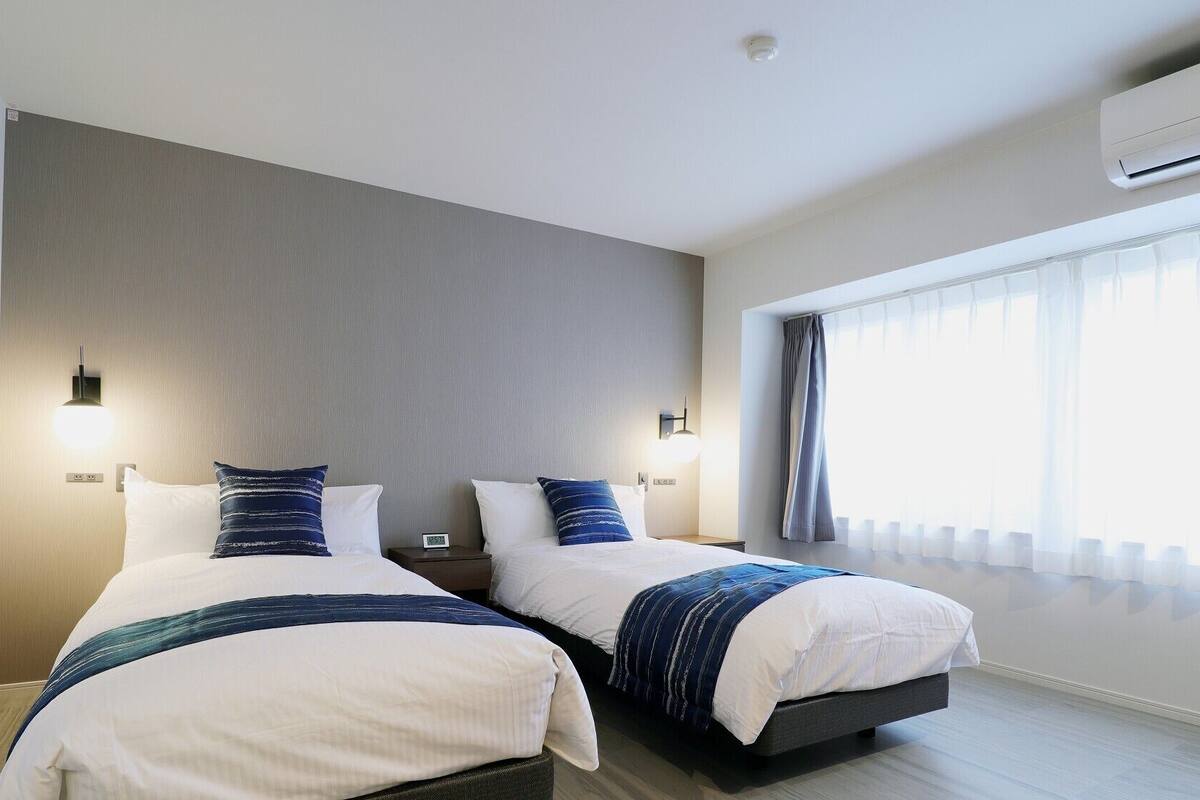 Une chambre d’hôtel avec deux lits, une grande fenêtre avec des rideaux, un appareil de climatisation et un luminaire fixé au mur.