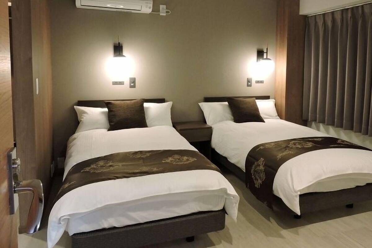 Une chambre d’hôtel avec deux lits, chacun doté d’une tête de lit, de tables de chevet et de lampes fixées au mur.