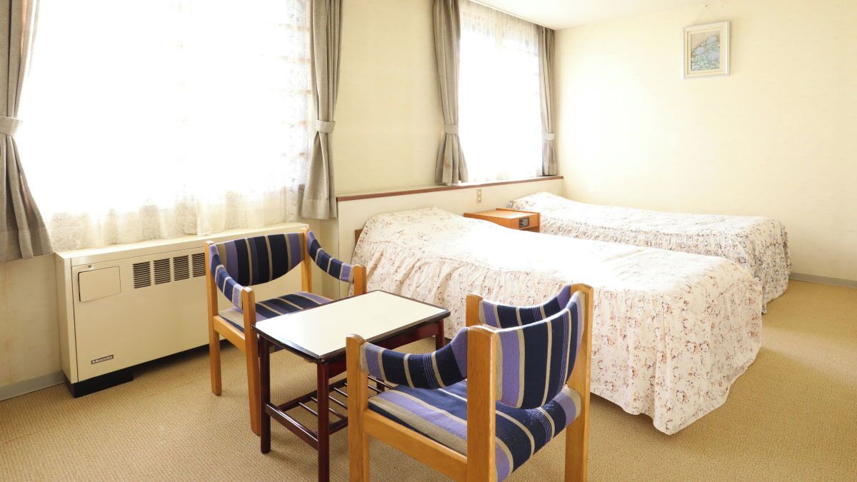 A hotel room with a bed, two chairs, a table, and a window with curtains.