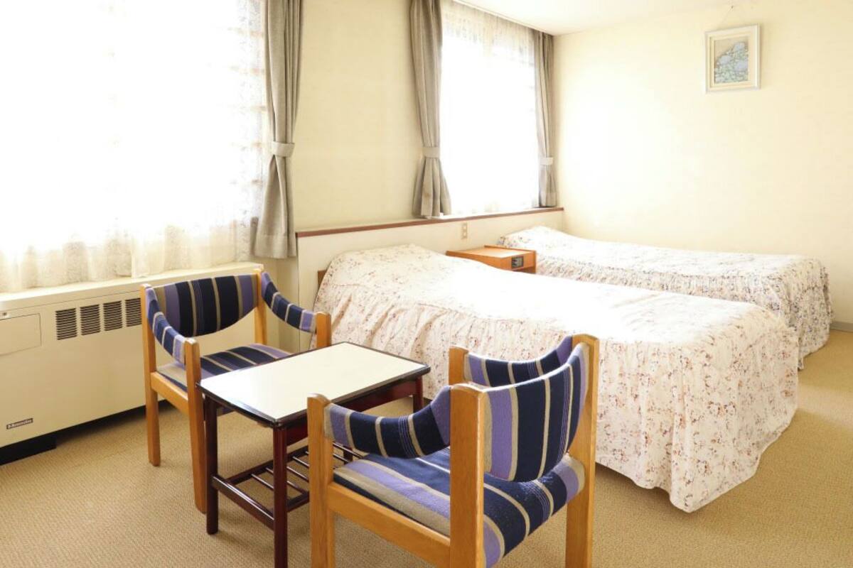 Une chambre d’hôtel avec un lit, deux chaises, une table et une fenêtre avec des rideaux.