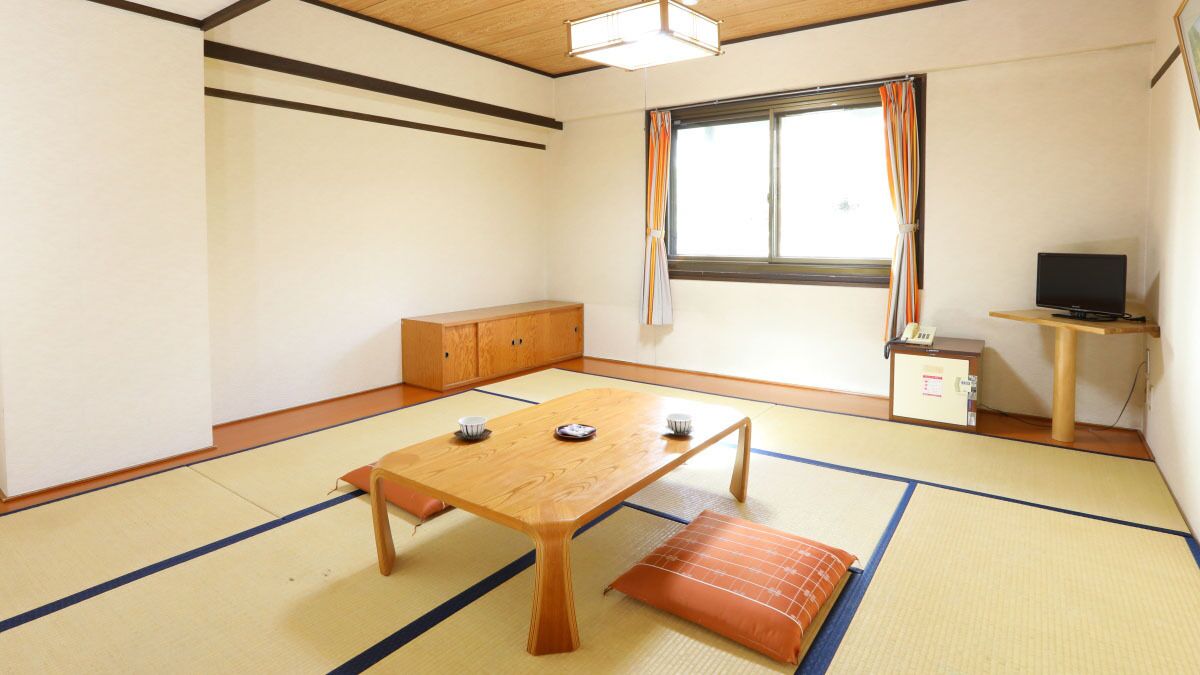 A traditional Japanese room with tatami flooring, a low wooden table, a cushioned bench, a cabinet, and a television on a small stand.