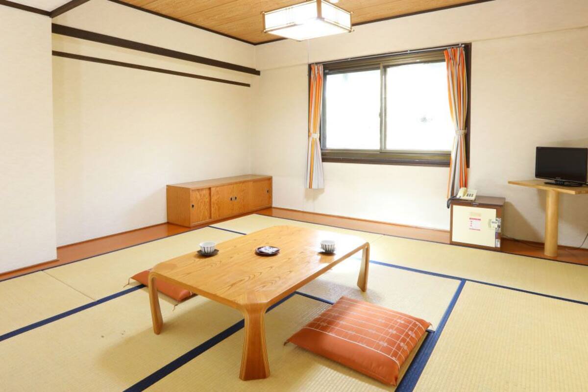 Une pièce de style japonais traditionnel, avec un sol recouvert de tatamis, une petite table en bois, un banc rembourré, un meuble et un téléviseur posé sur un petit meuble.