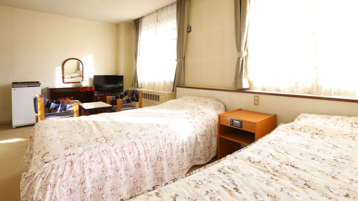 A hotel room with two beds, a desk, a television, and a small refrigerator.
