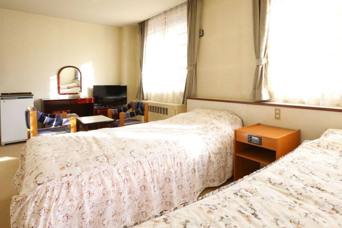 Une chambre d’hôtel avec deux lits, un bureau, une télévision et un petit réfrigérateur.