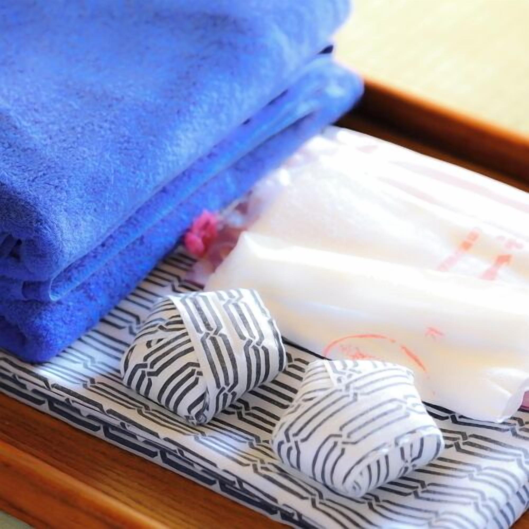 A neatly folded blue towel, a white and black striped pillow, and a white pillow with a red design on a wooden surface.