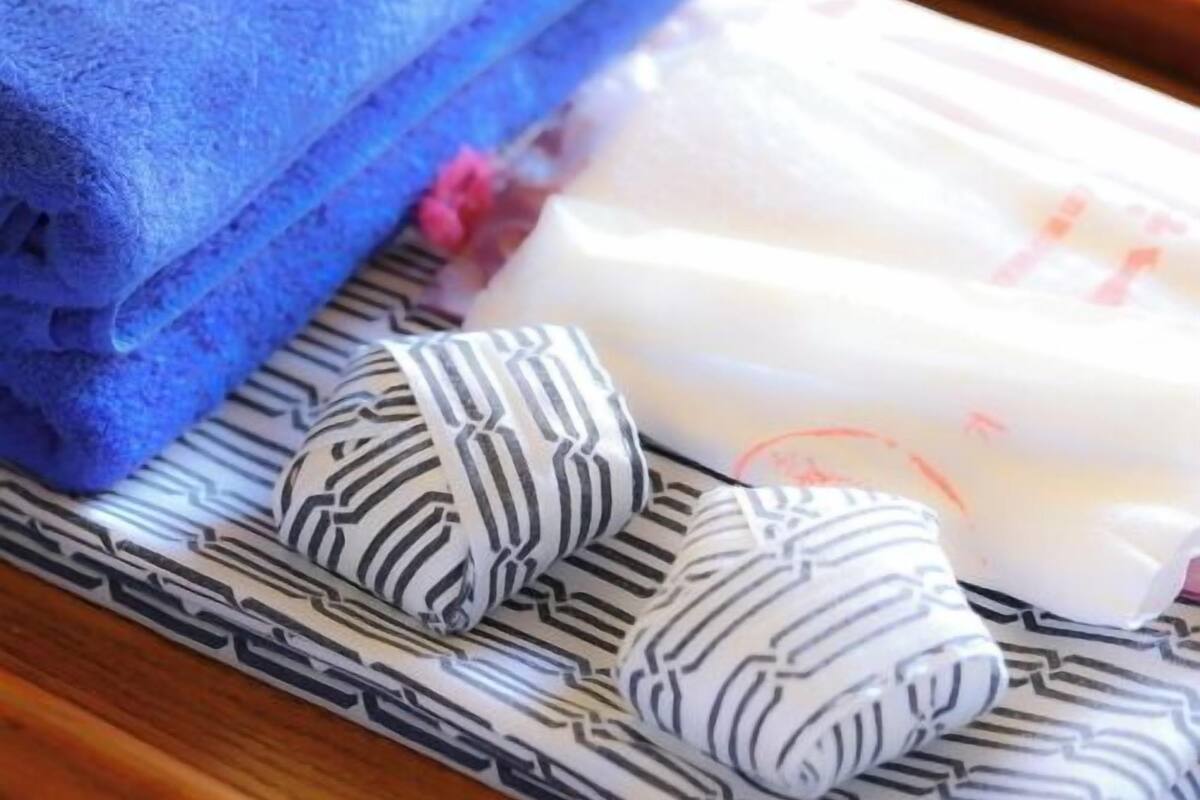Une serviette bleue soigneusement pliée, un coussin rayé noir et blanc et un coussin blanc orné d’un motif rouge, le tout posé sur une surface en bois.