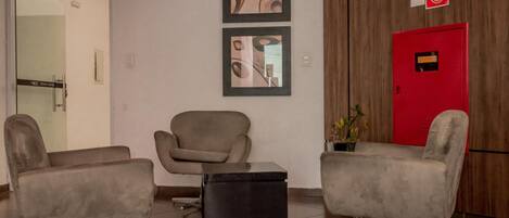 A lobby with three modern armchairs, a small black ottoman, and a red fire safety cabinet.