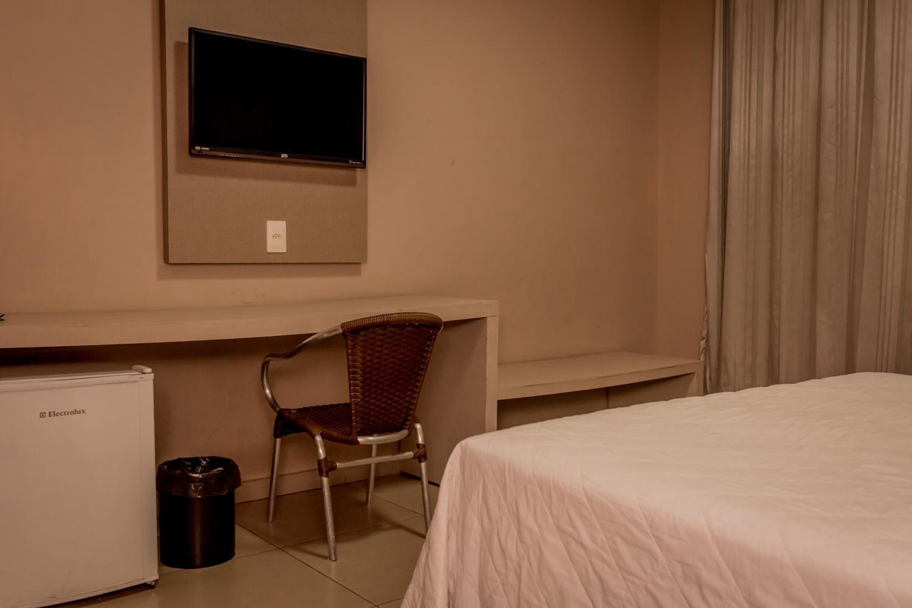 A hotel room with a bed, a desk with a chair, a television, and a refrigerator.