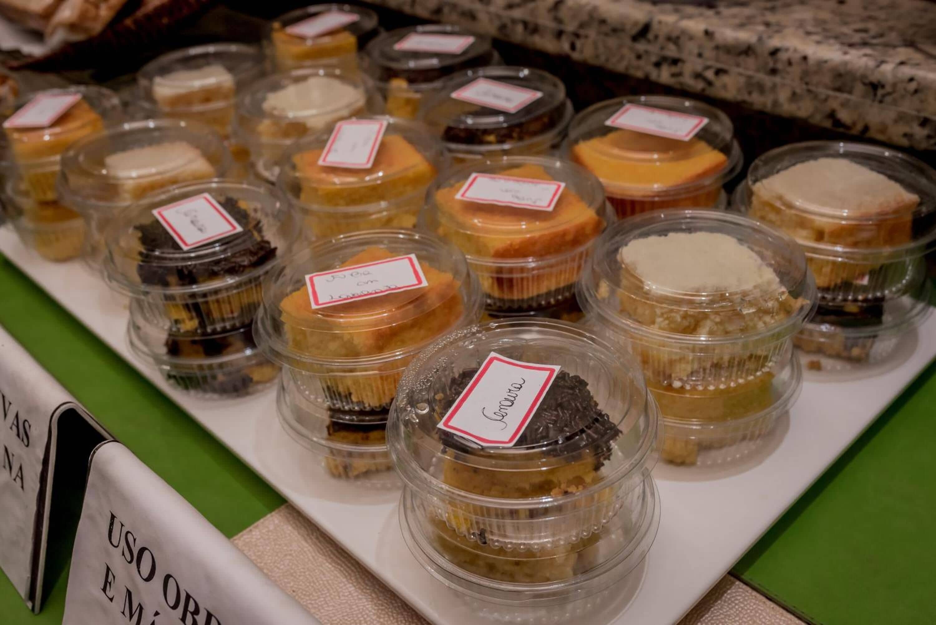 Una exhibición de diversos postres en recipientes transparentes con etiquetas, dispuestos sobre una mesa.