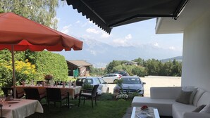 Une terrasse extérieure avec une table dressée pour le repas, un parasol rouge et un canapé blanc.